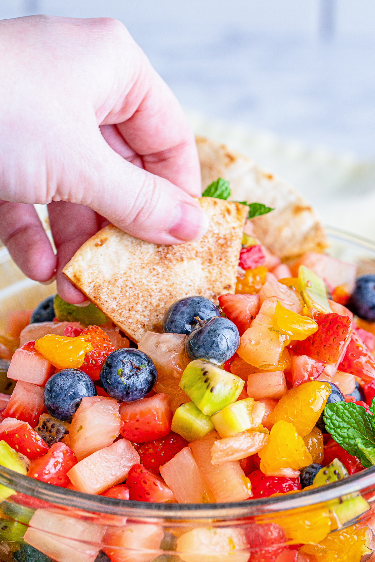 a hand holding a tortilla into fruit salsa
