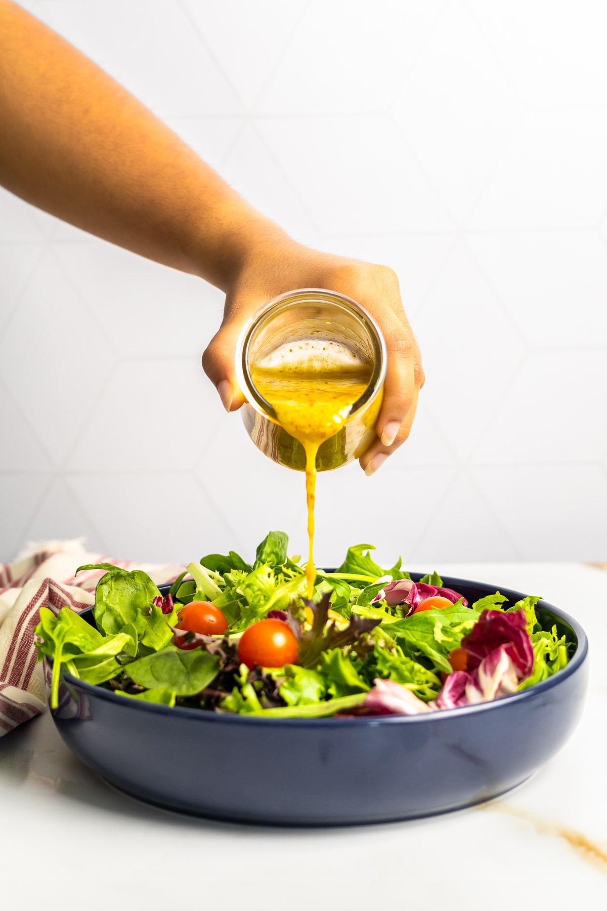 a hand pouring Honey Mustard Dressing Recipe over a large salad