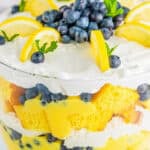 A layered lemon blueberry trifle in a glass dish topped with fresh blueberries and lemon.