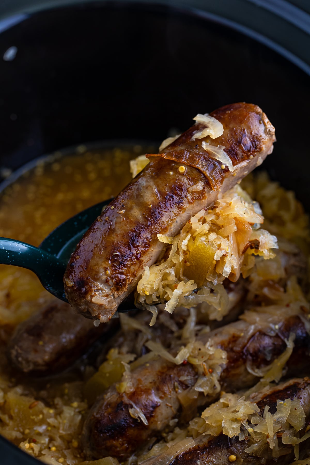 a spoon holding up Brats and Sauerkraut over slow cooker in air