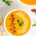 An overhead bowl of creamy carrot soup topped with toasted pecans and parsley.