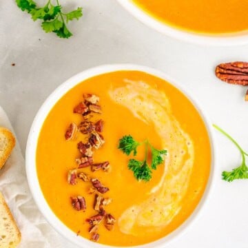 An overhead bowl of creamy carrot soup topped with toasted pecans and parsley.