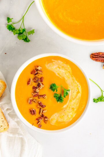 An overhead bowl of creamy carrot soup topped with toasted pecans and parsley.