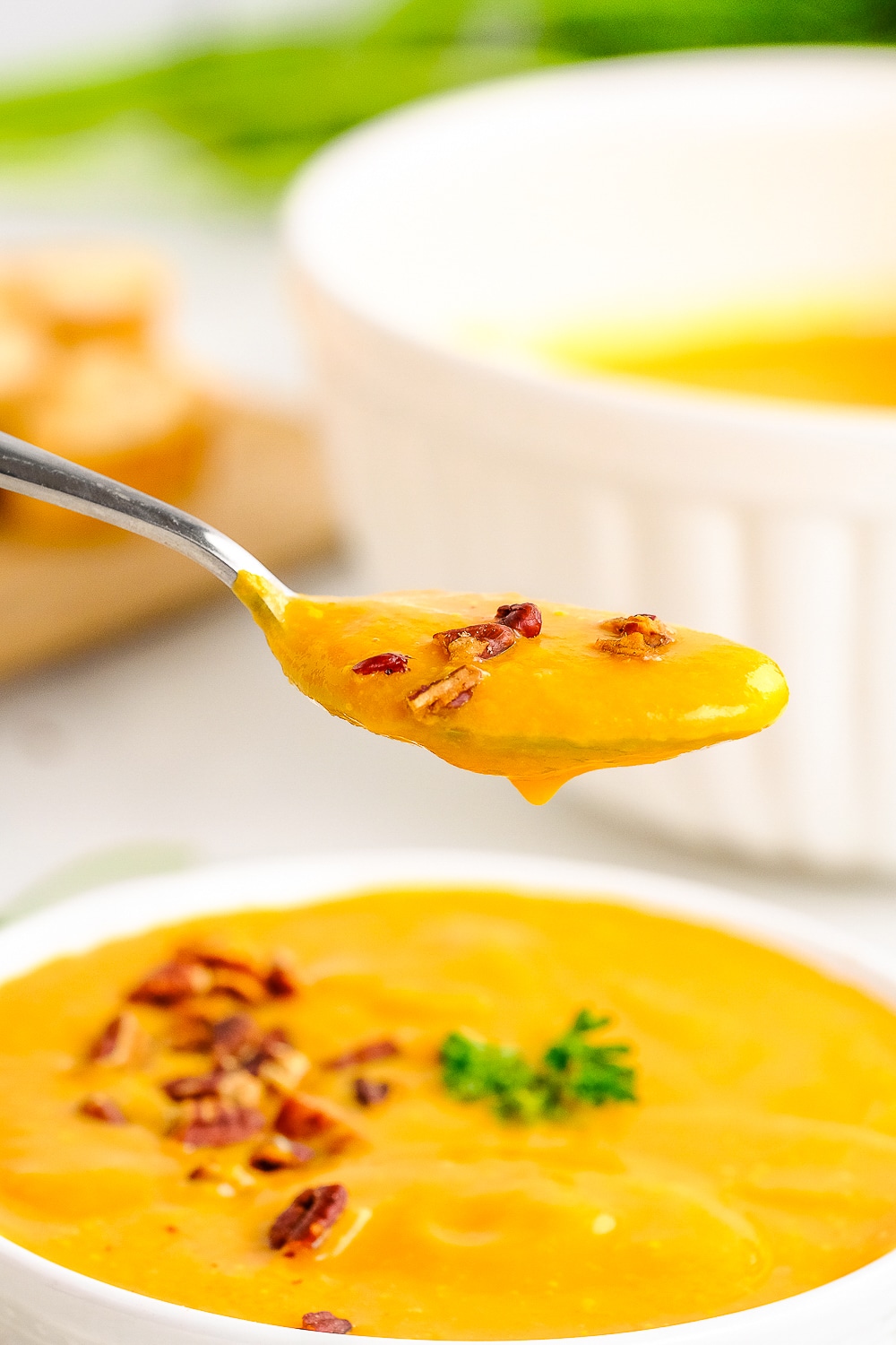 a spoon holding up a bite of carrot soup in air