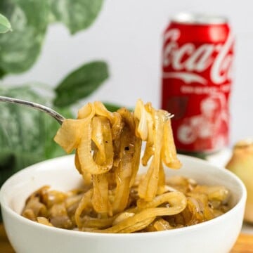 A fork lifting glossy Caramelized Coca-Cola Onions from a white bowl with a Coke can behind it.