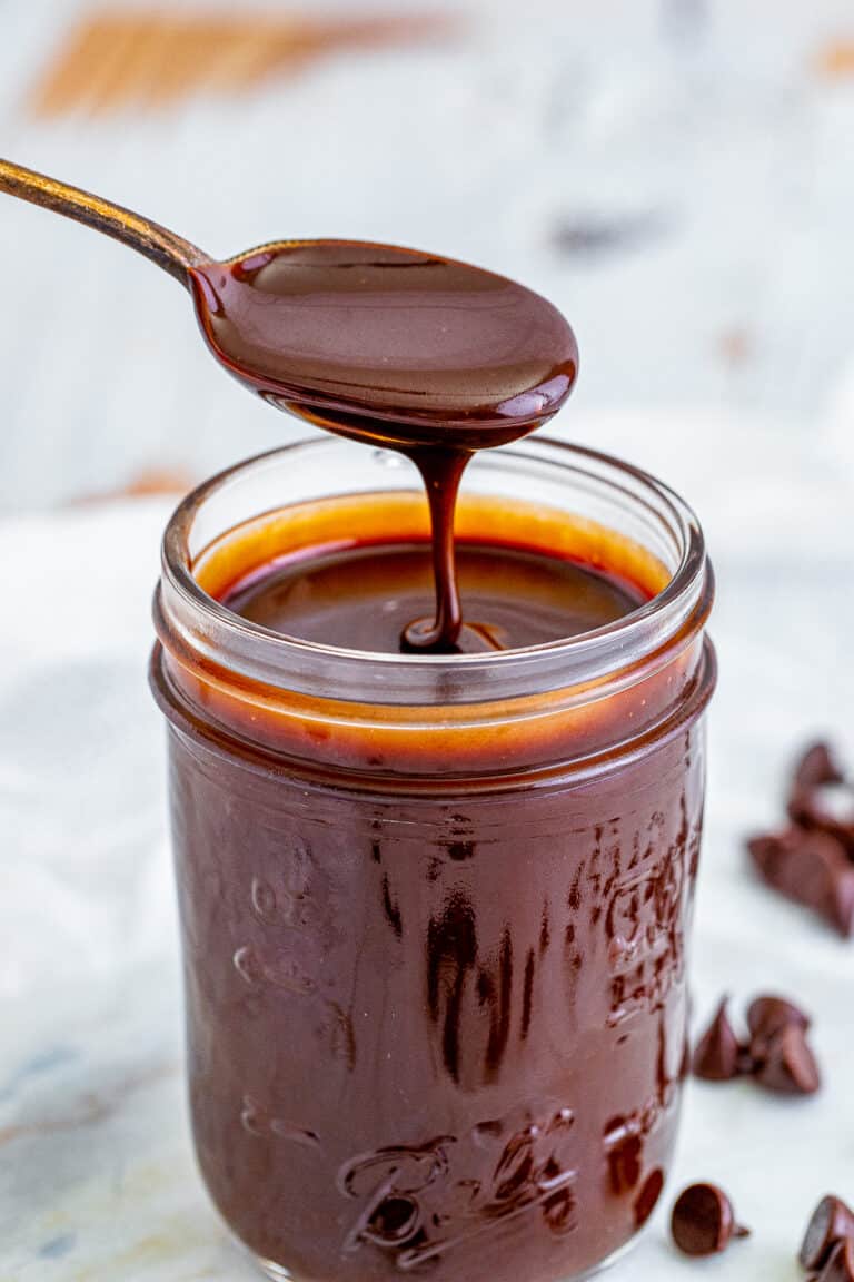 Hot fudge sauce dripping off a spoon over a mason jar.