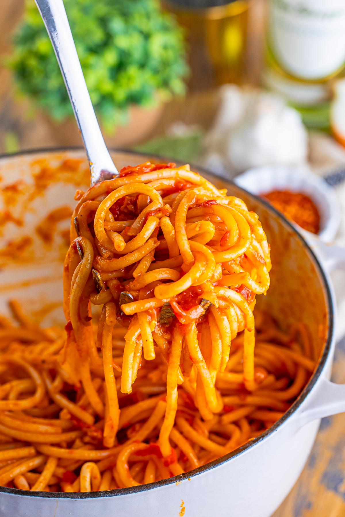a slotted spoon holding up some Bucatini all Amatriciana over a pot