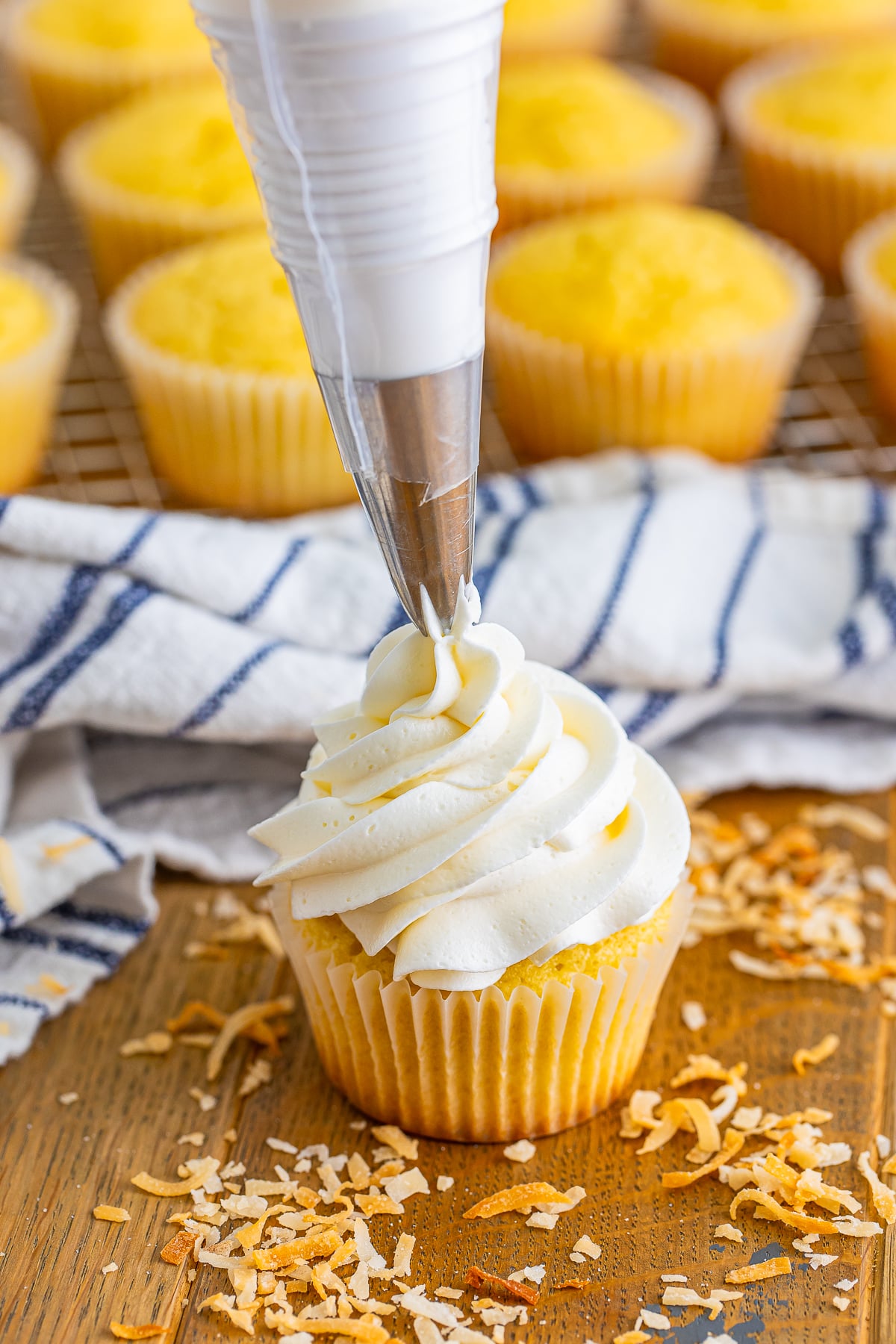 a piping bag adding Coconut Frosting to the top of a cupcake