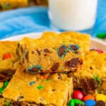 Thick and chewy monster cookie bars on a white plate with a glass of milk.
