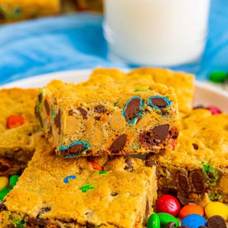 Thick and chewy monster cookie bars on a white plate with a glass of milk.