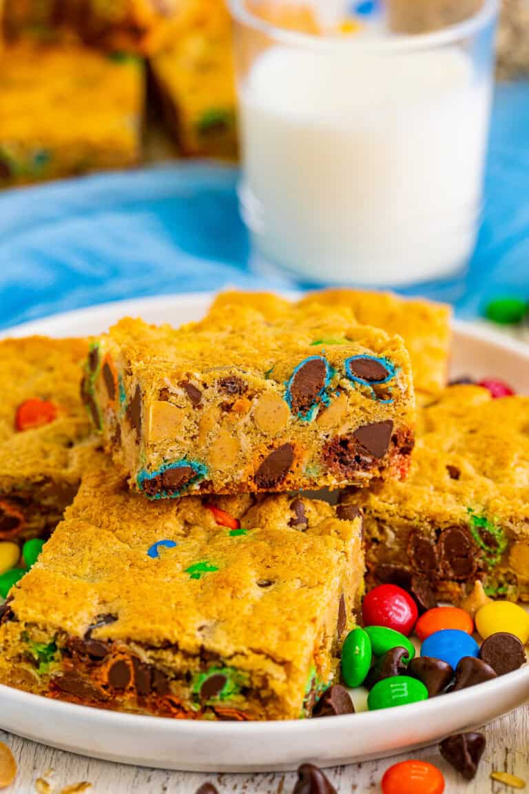 Thick and chewy monster cookie bars on a white plate with a glass of milk.