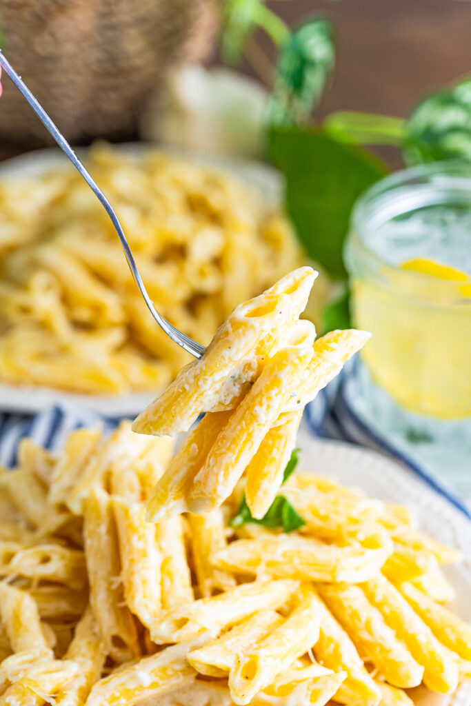 a fork holding up a bite of Alfredo Sauce with Penne Pasta in air