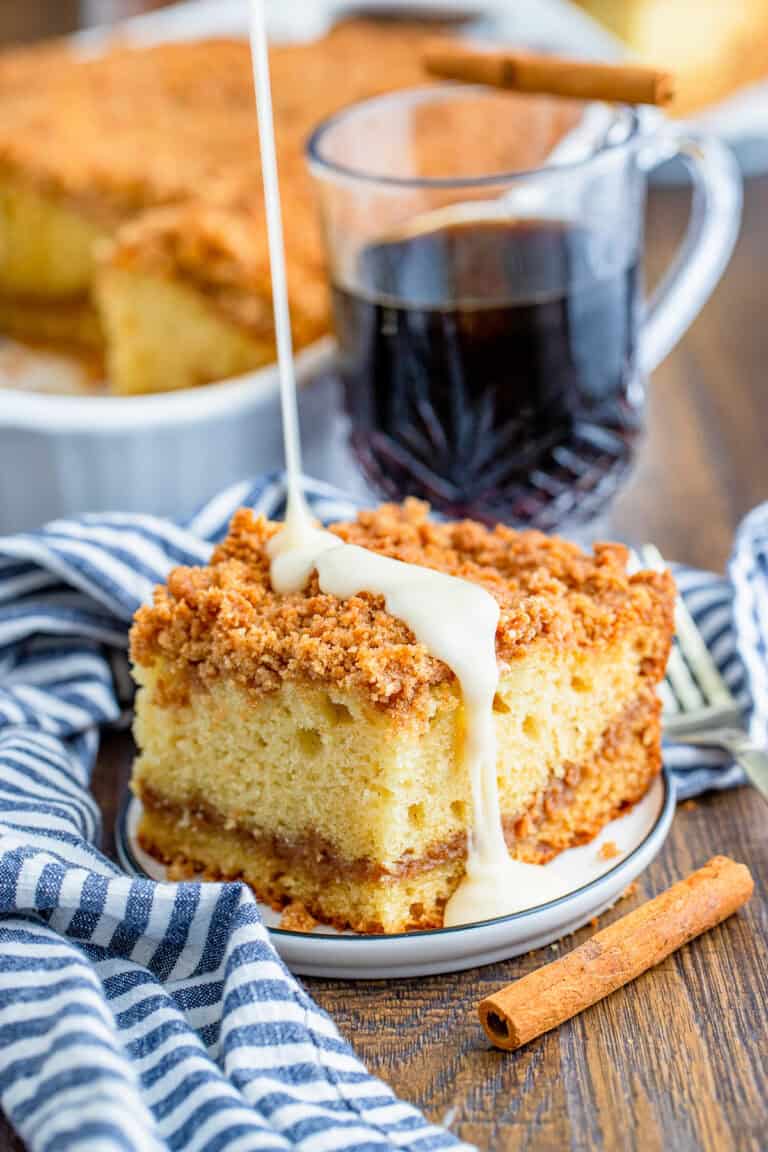 A slice of sour cream coffee cake with cinnamon crumble and a sour cream glaze drizzle on a plate.