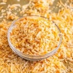 A bowl of golden toasted coconut with more scattered on a wooden board.