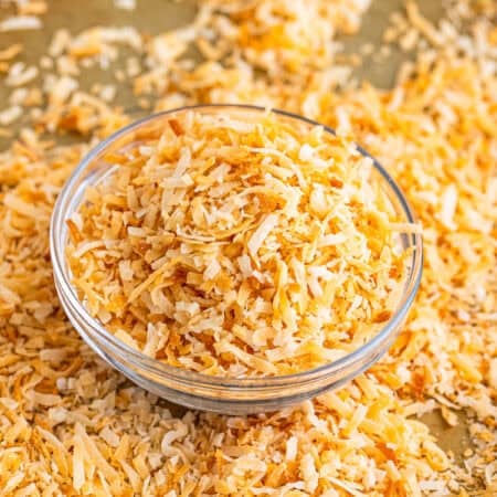 A bowl of golden toasted coconut with more scattered on a wooden board.