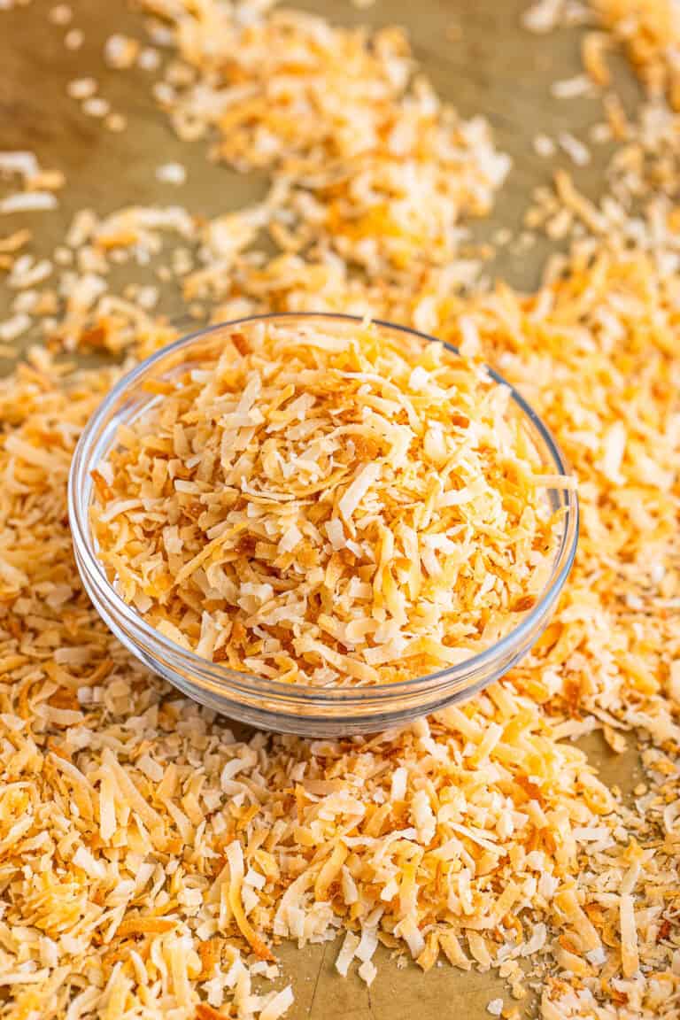 A bowl of golden toasted coconut with more scattered on a wooden board.