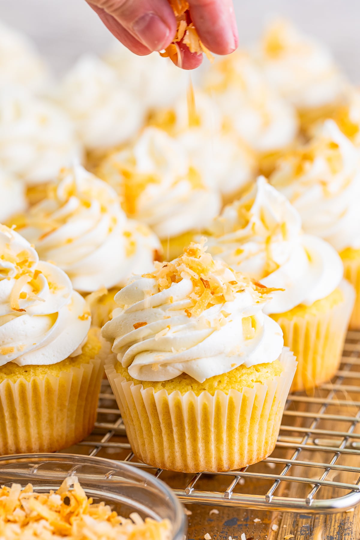 a hand sprinkling toasted coconut on top of cupcakes