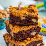 A stack of three thick and chewy Butterfinger brownies topped with peanut butter and crushed candy bars.