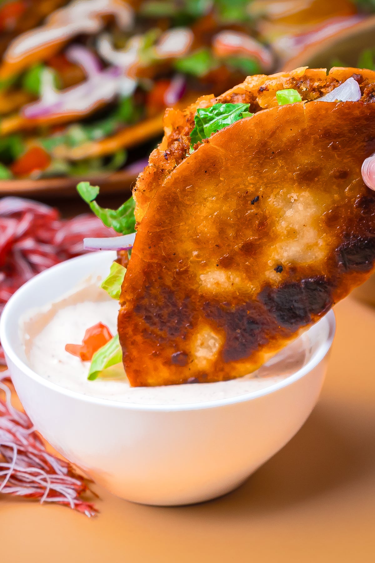 a hand dipping Crispy Tacos into sauce