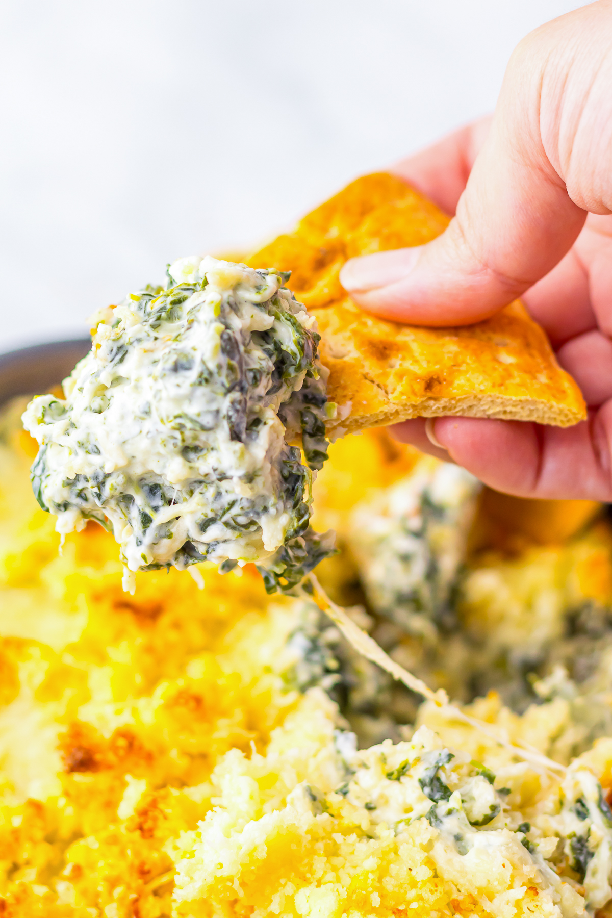 a hand scooping out hot spinach dip in air on a pita 