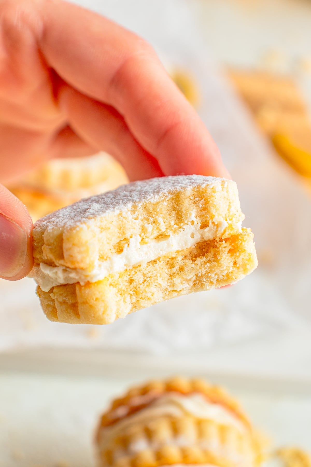 a hand holding up Lemon Sandwich Cookies in air with a bite taken out