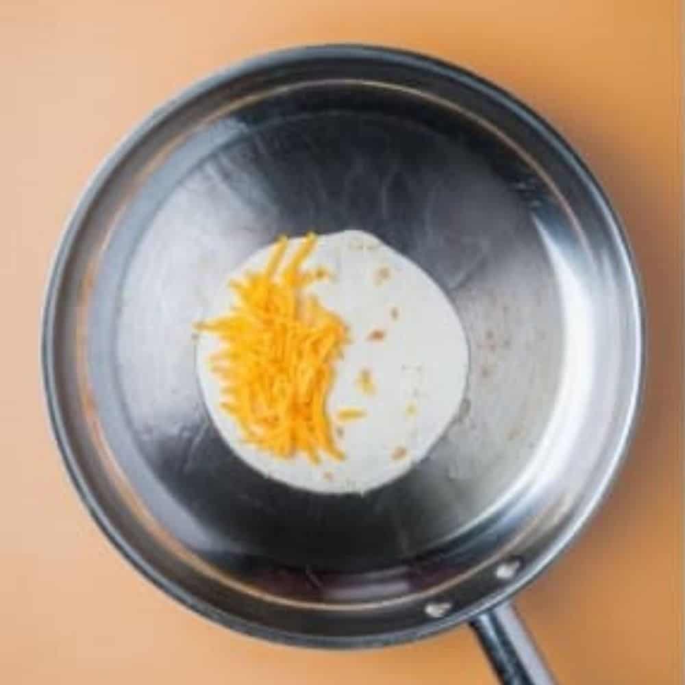 tortilla in a saucepan with shredded cheese.