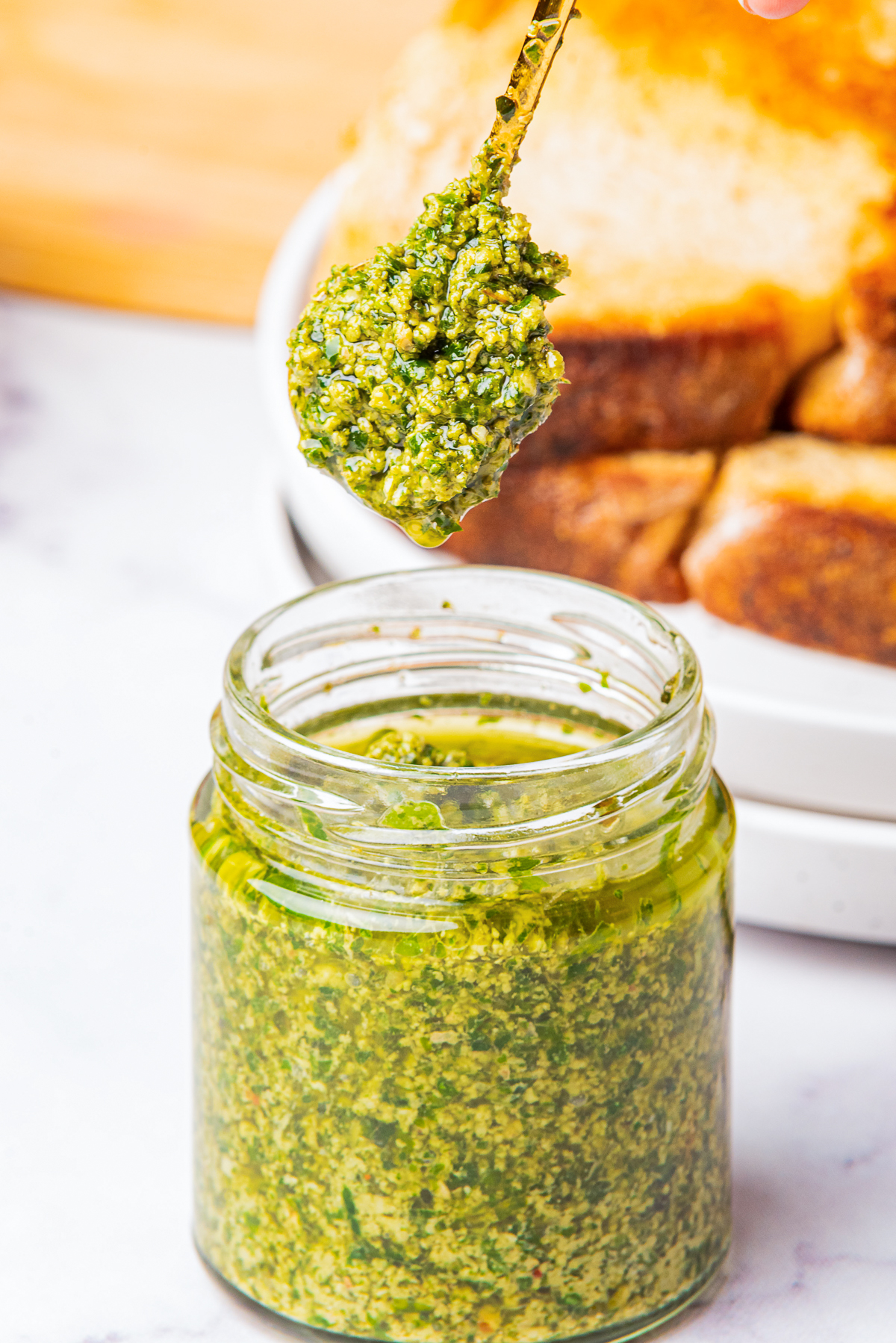 a spoon holding up Pesto sauce with walnuts over a glass jar