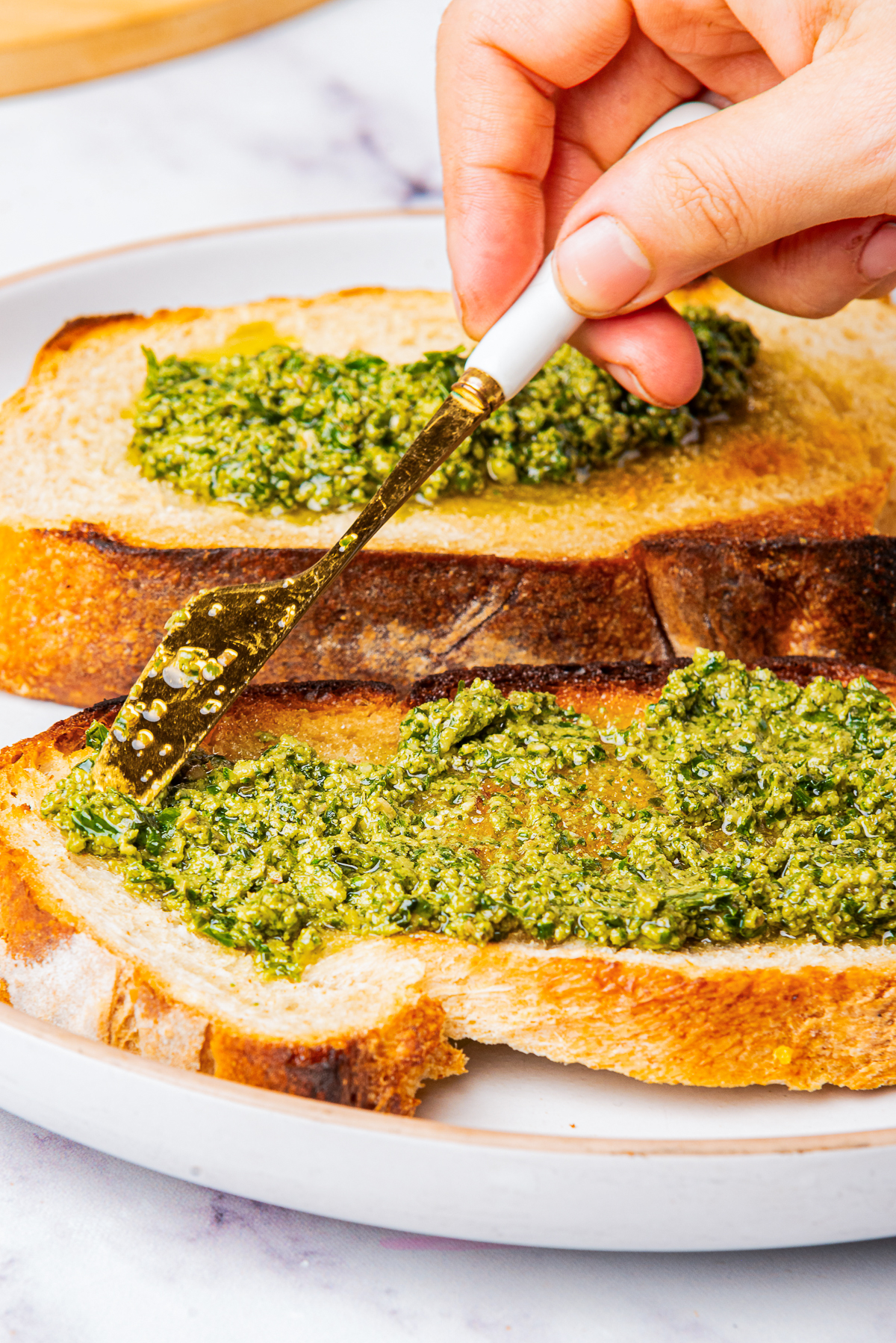 Pesto sauce with walnuts being spread on toast with a knife