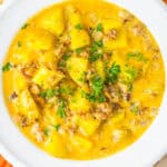 A white bowl of creamy sausage potato soup topped with fresh parsley.