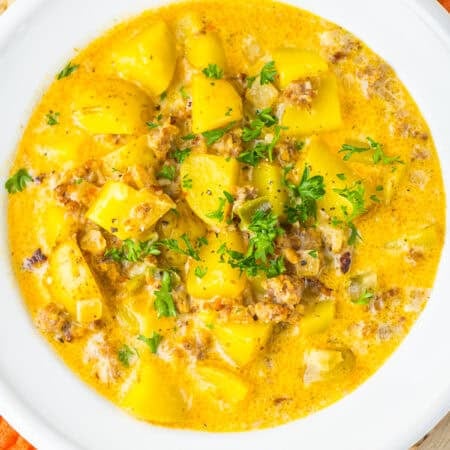 A white bowl of creamy sausage potato soup topped with fresh parsley.
