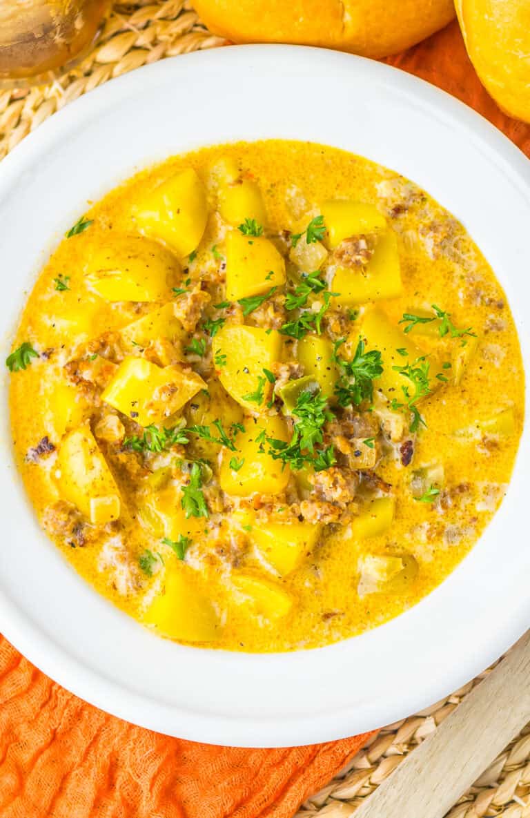 A white bowl of creamy sausage potato soup topped with fresh parsley.