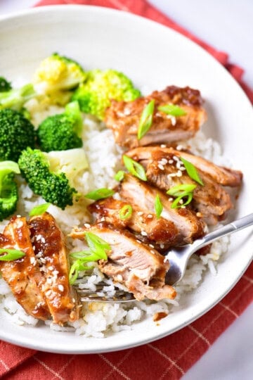 Copycat Panda Express Teriyaki Chicken Recipe served in a white bowl with sliced chicken thighs glazed in teriyaki sauce, white rice, and steamed broccoli on a red napkin.