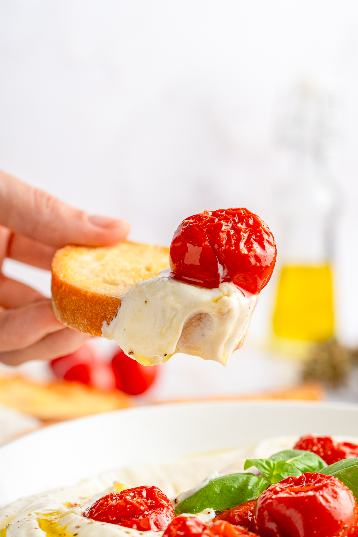 a hand holding up a piece of bread in air with Whipped Ricotta Cheese and a tomato