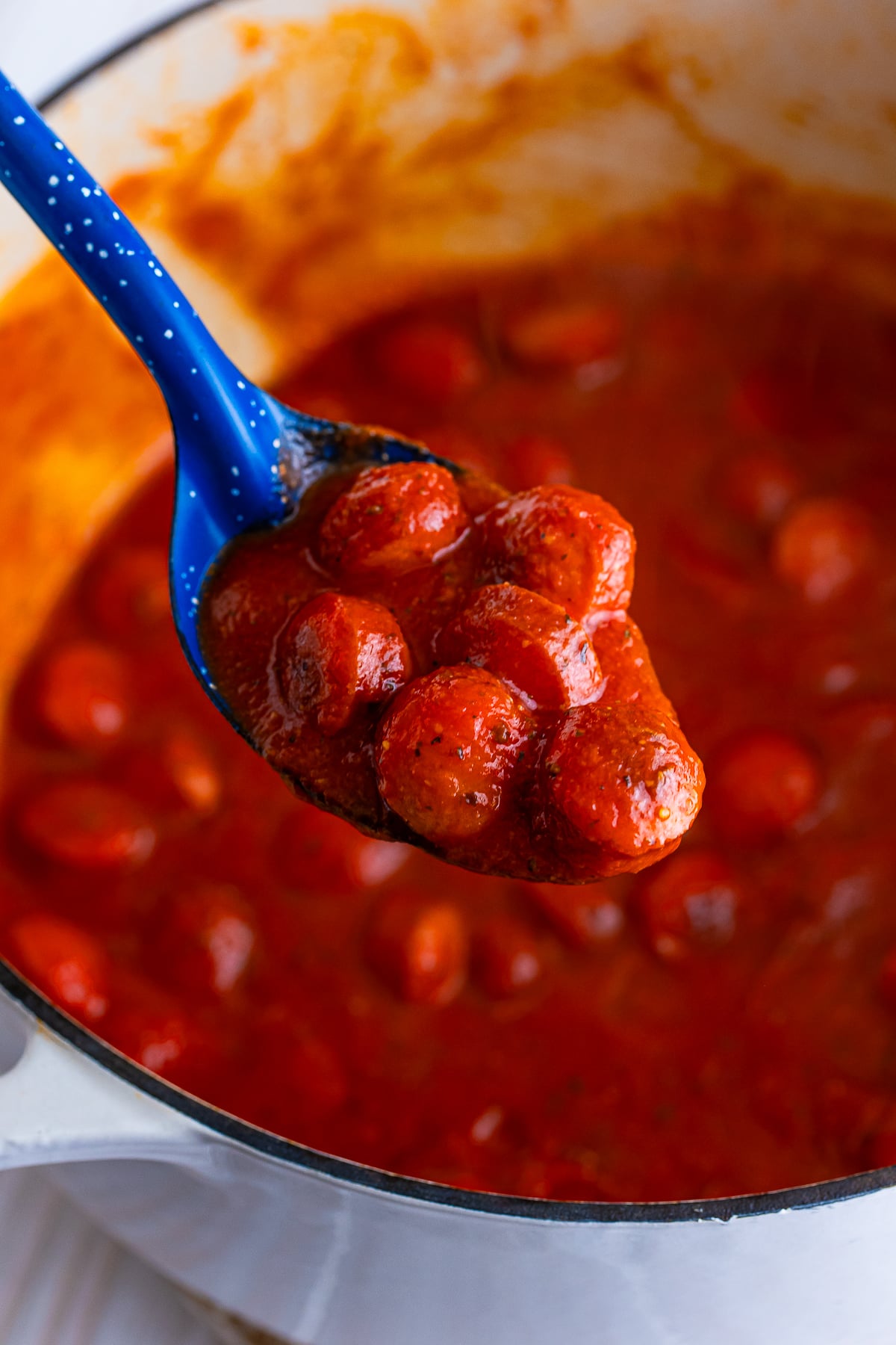 a spoon holding up some of the Hot Dogs Spaghetti sauce over the pot