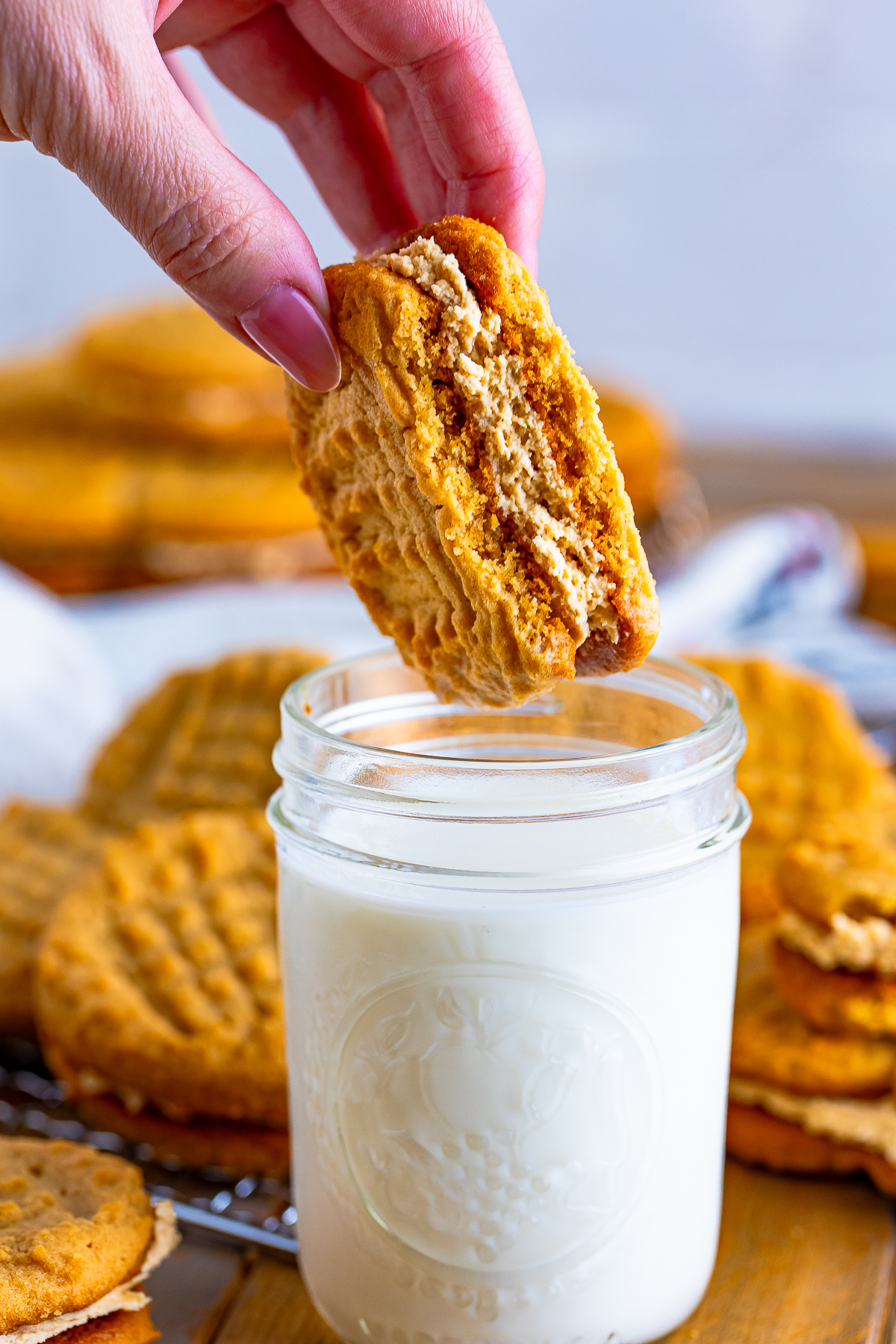 a hand holding up half a Nutter Butter Cookies over a glass of milk