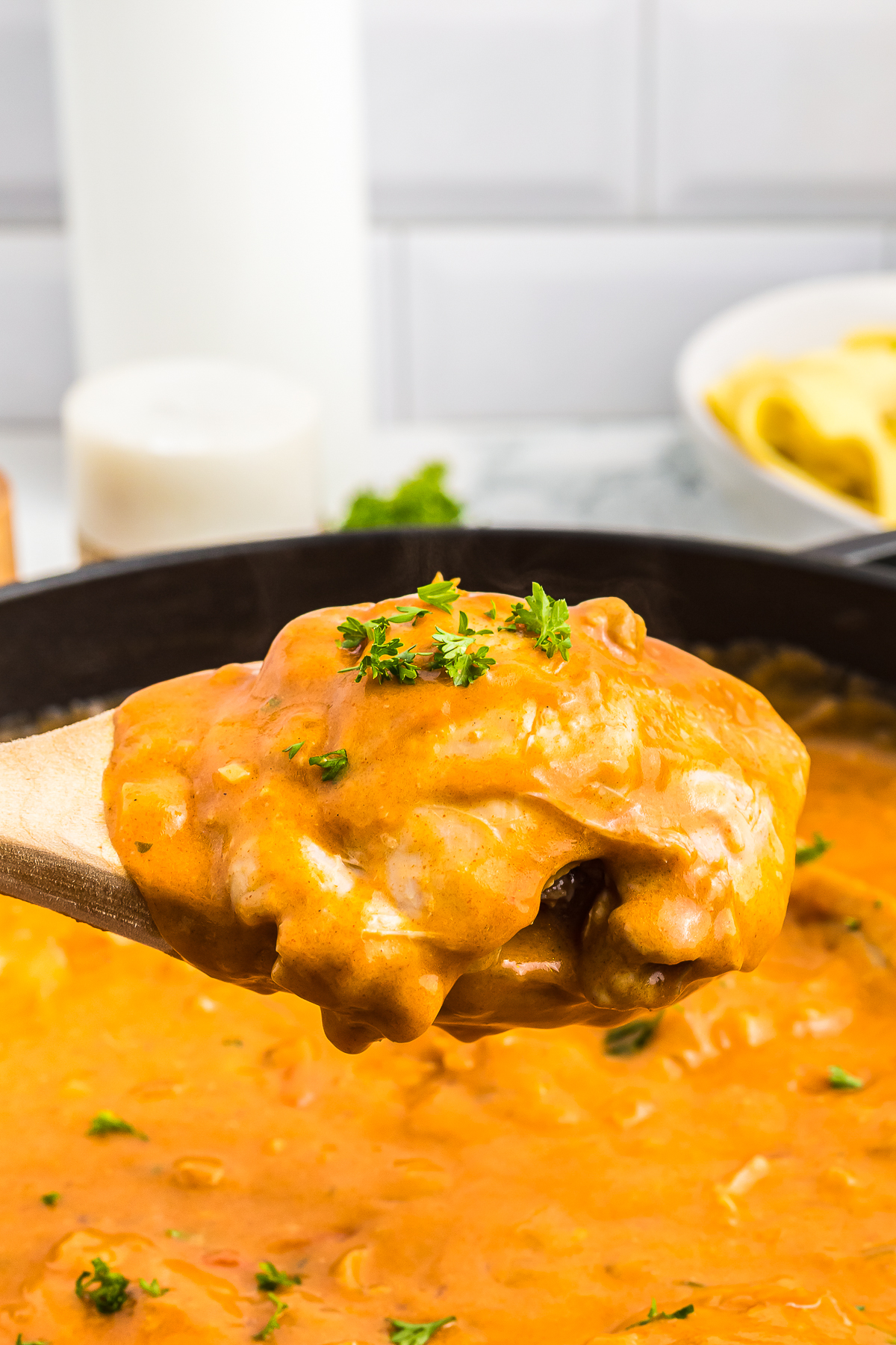 a spoon holding up a piece of Paprika Chicken over skillet