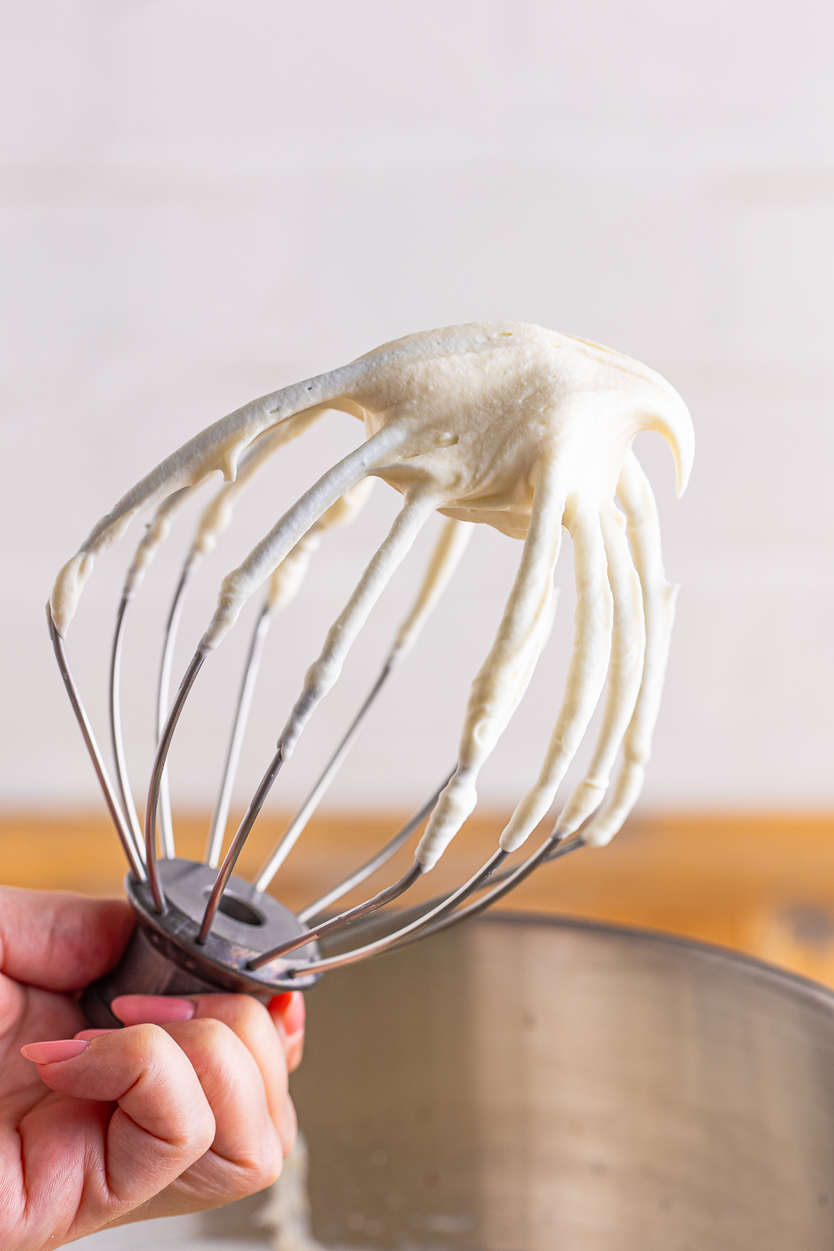 a hand holding up a whisk with Whipped Cream Cream Cheese Frosting on it