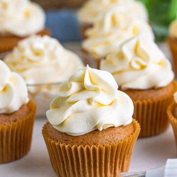 Cupcakes topped with swirls of whipped cream cheese frosting and a piping bag.