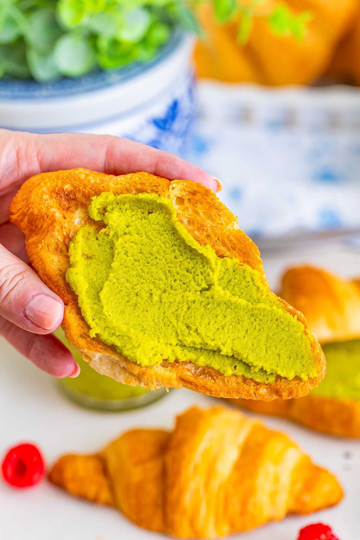 a hand holding up piece of toasted croissant with Pistachio Spread on it