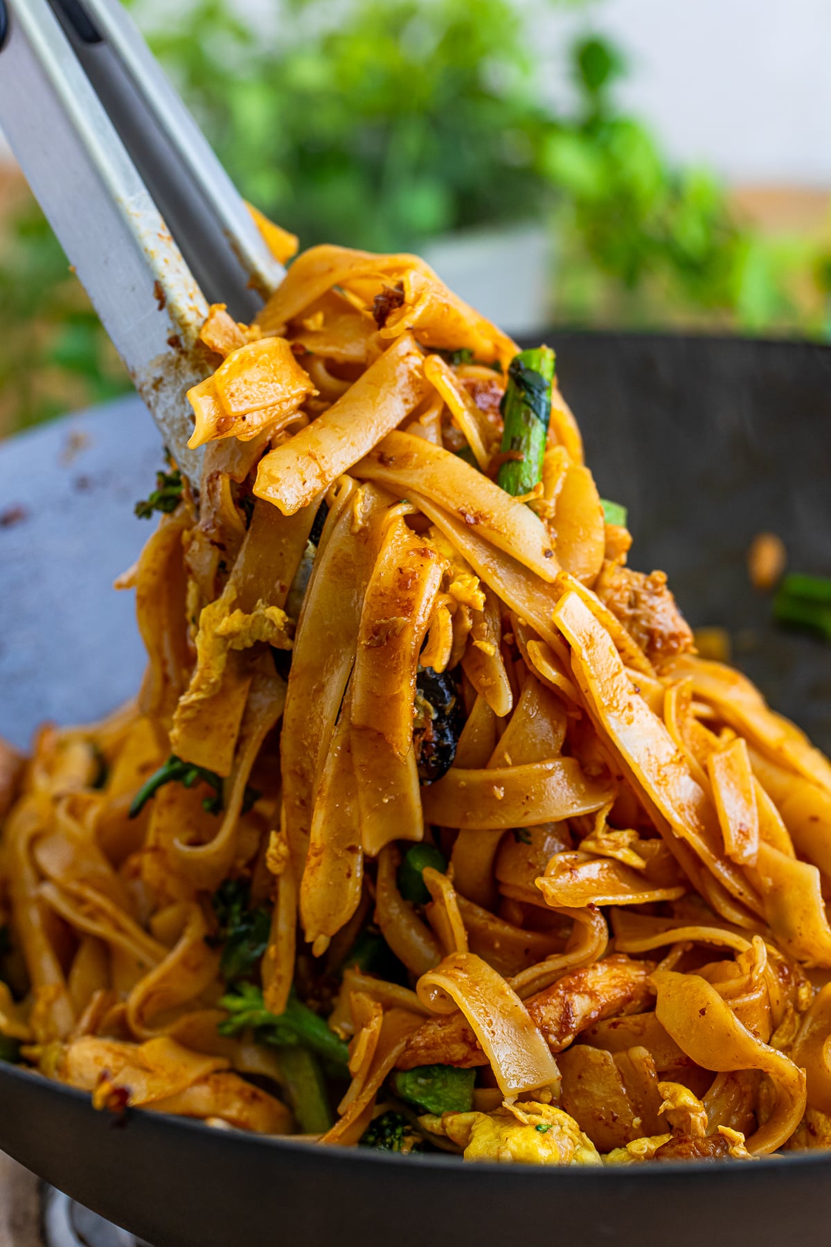 a pair of tongs grabbing some Thai Pad See Ew out of the wok