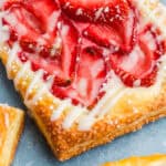 A close up of a flaky strawberry cream cheese danish topped with fresh strawberries and a sweet glaze.