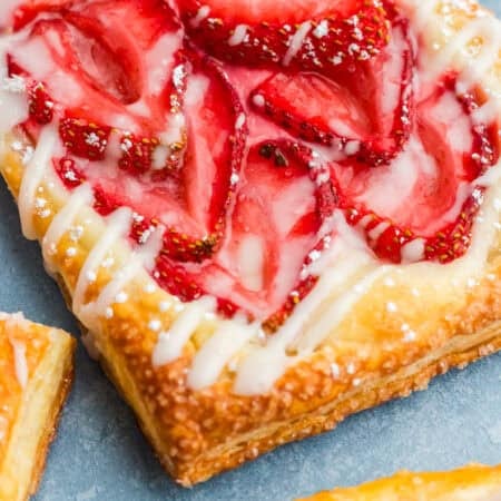 A close up of a flaky strawberry cream cheese danish topped with fresh strawberries and a sweet glaze.