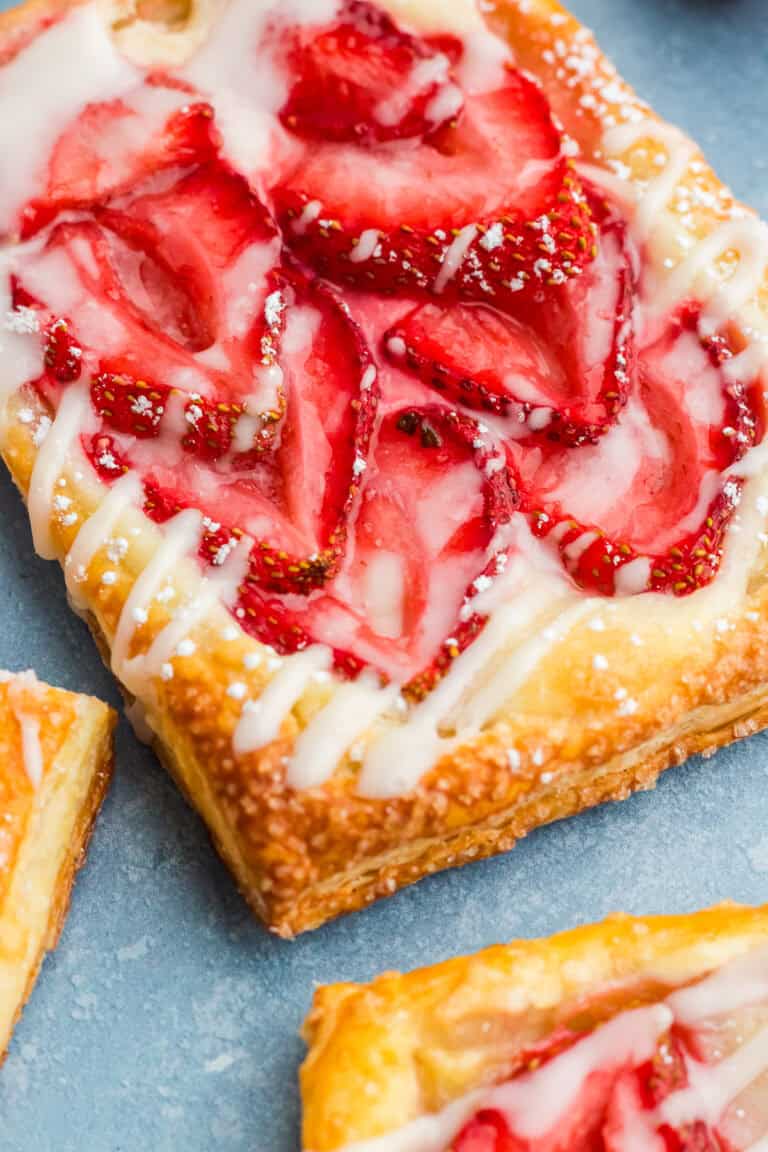 A close up of a flaky strawberry cream cheese danish topped with fresh strawberries and a sweet glaze.