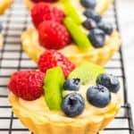 A mini fruit tartlet topped with raspberries, blueberries, and kiwi on a cooling rack.