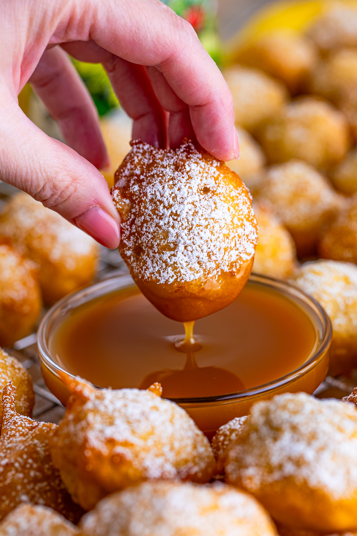 a hand dipping Banana Fritters into caramel sauce