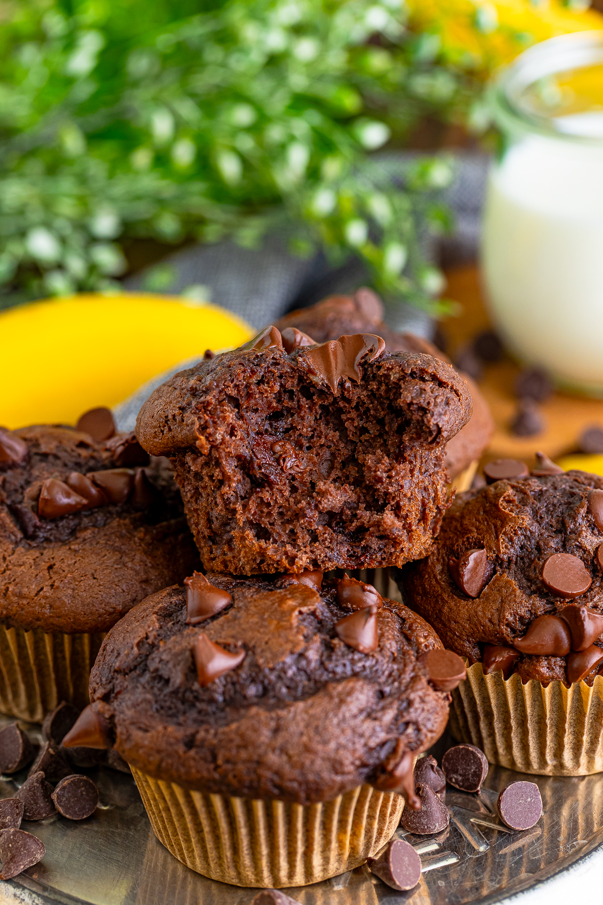 Chocolate Banana Chocolate Chip Muffins stacked on a metal tin, the one on top has a bite taken out