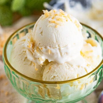 A scoop of Creamy Coconut Ice Cream in a green glass dish topped with toasted coconut.