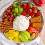 Easy Cream Cheese Fruit Dip Recipe with Cool Whip served in a pink bowl on a large wooden board with fresh strawberries, grapes, pineapple, apples, and graham crackers.