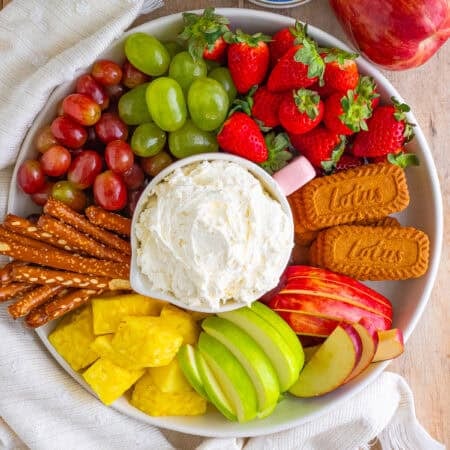 Easy Cream Cheese Fruit Dip Recipe with Cool Whip served in a pink bowl on a large wooden board with fresh strawberries, grapes, pineapple, apples, and graham crackers.