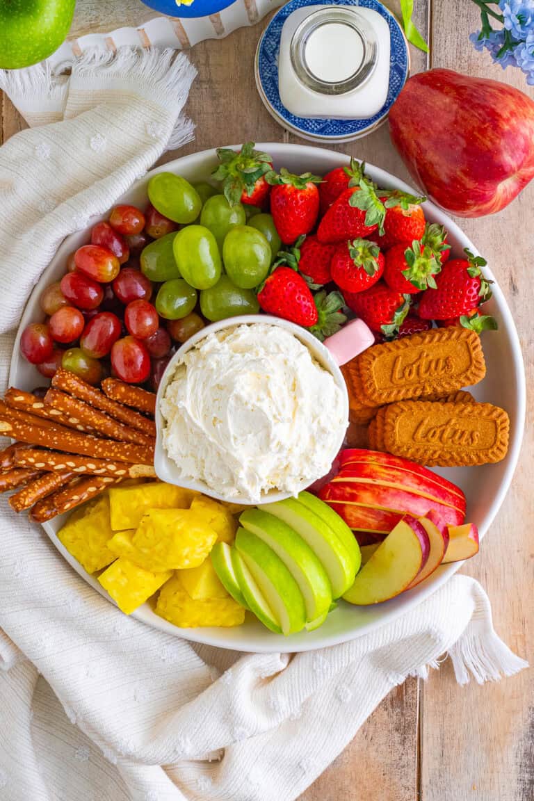 Easy Cream Cheese Fruit Dip Recipe with Cool Whip served in a pink bowl on a large wooden board with fresh strawberries, grapes, pineapple, apples, and graham crackers.